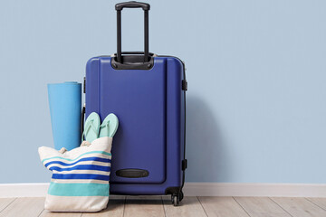 Packed suitcase and beach bag with yoga mat and flip-flops near blue wall