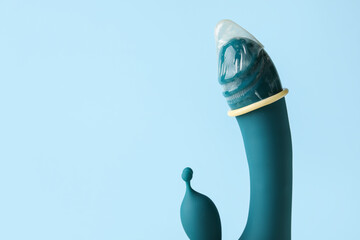 Vibrator with condom on color background, closeup