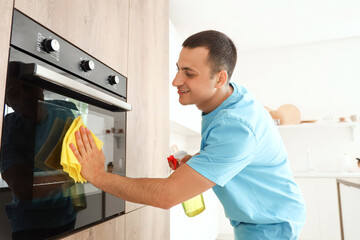 Young man cleaning oven in kitchen