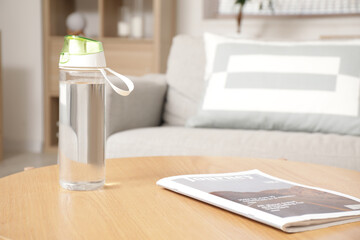 Sports water bottle and magazine on table in living room, closeup