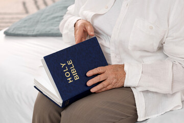 Senior woman with Bible sitting on bed at home, closeup