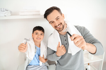 Obraz premium Happy father and his little son holding razors with towels in bathroom