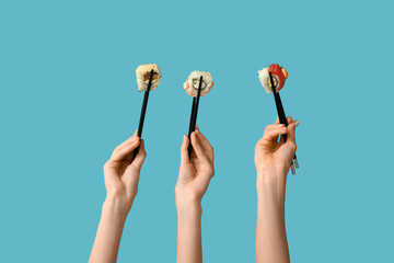 Female hands holding chopsticks with different tasty sushi rolls on blue background