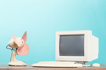 Retro cooling fan and desktop computer monitor, keyboard and mouse on wooden table front mint blue...