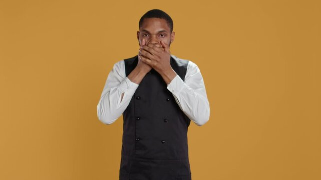 Restaurant staff covering his eyes, mouth and ears against evil in studio, presenting three wise monkeys metaphor. Waiter doesnt see, hear or speak as a concept, hospitality industry. Camera B.