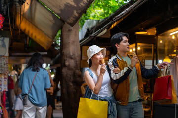 Obraz premium Happy Asian man and woman couple enjoy and fun outdoor lifestyle travel in the city shopping and eating street food together at weekend street market in Bangkok, Thailand on summer holiday vacation.