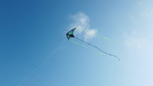 Blue and green kite with three tails flying in a clear sky from below