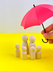 small umbrella with wooden family peg dolls for protection with copy space. Family protection and insurance coverage concept. The insurance agent presents protection model that symbolize the coverage.