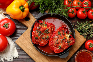 Tasty stuffed peppers in dish and ingredients on wooden table, flat lay