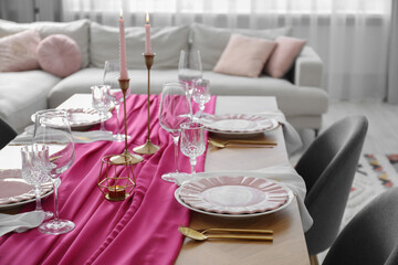 Beautiful table setting with burning candles and pink accent in dining room