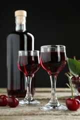 Bottle and glasses of delicious cherry liqueur with juicy berries on wooden table against dark background
