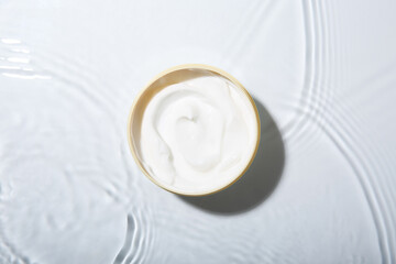 Cosmetic product. Jar with cream in water on light background, top view