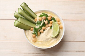 Tasty hummus with chickpeas, cucumber and lime in bowl on wooden table, top view