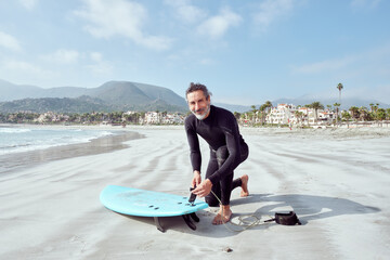 mature surfer man on the beach shore preparing to go in to surf the waves