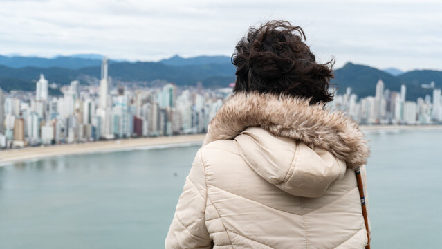 Young white brunette woman contemplating the view of the beachfront with large buildings in the background and the sea.