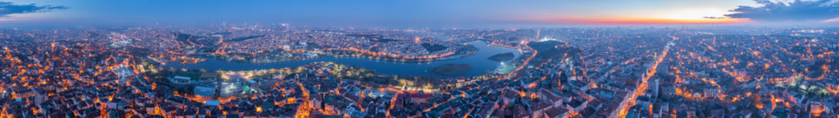 Areal view of sprawling Istanbul cityscape illuminated at dusk reveals bustling historic city around Bosphorus Strait. Twilight sunset sky transitioning from day to night, city lights twinkling below.