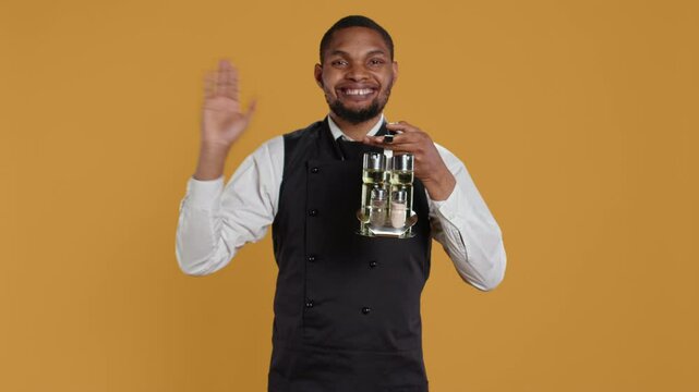 Happy friendly waiter waving hello and welcoming clients at table, holding a cruet set with condiments ready to serve customers. Cheerful lovely staff greeting people at restaurant. Camera B.