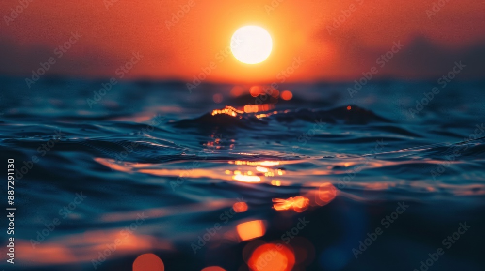 Poster waves lap gently at the surface of the ocean as the sun sets behind them, creating a blurred, golden