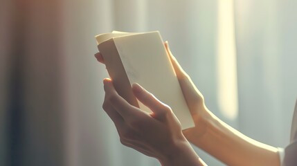 Female hands holding closed book with blank cover on light background.