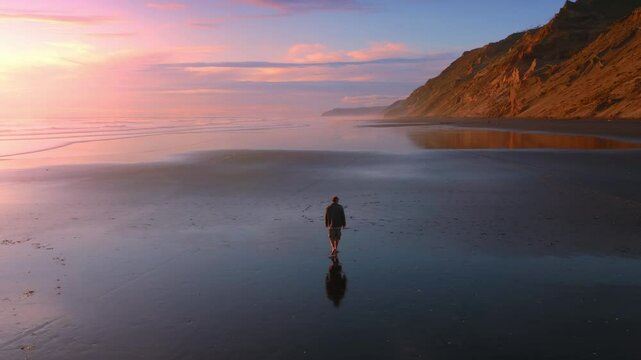 Man walking along the beach at low tide with the shore reflecting the sky giving the feeling of heaven. Hamiltons Gap, Awhitu Peninsula, Auckland, New Zealand.