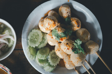 Meatballs toasted on dish and a spicy sauce decorated with coriander and cucumber placed on the table. Grill pork balls at street food in Thailand. Toasted meatballs topped with spicy sauce