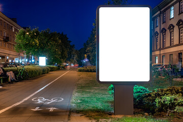 Blank White Billboard Mockup On Pedestrian Street Next To Bike Path At Night. Advertising Poster Lightbox For Commercial Branding