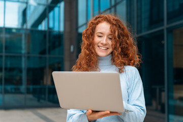 Smiling Woman With Red Hair Using Laptop Outside Modern Building