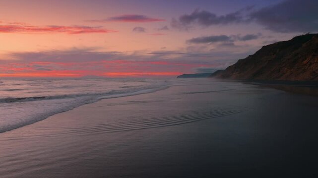 Cliff going into the ocean and sandy beach at sunset. Hamiltons Gap, Awhitu Peninsula, Auckland, New Zealand.