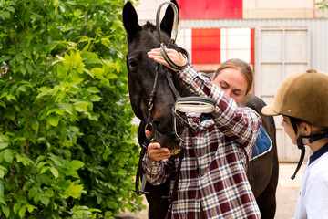Woman adjusting bridle on horse while interacting with rider.