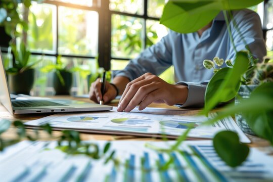 Businessperson analyzing financial documents and ESG amidst lush indoor plants in sunny office setting. Sustainable business practices, green office, eco-friendly workplace, financial analysis concept