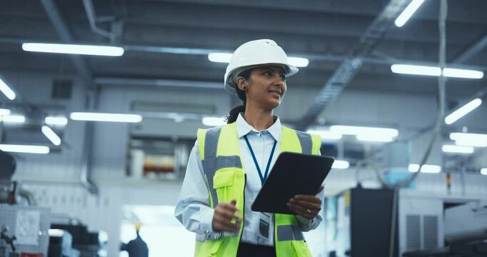 Portrait of a Latin Female Worker in a White Hard Hat Walking Through a Modern, Well-lit Factory, Inspecting Advanced Industrial Machinery, Checking Equipment, Overviewing Production