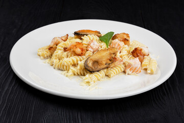 Seafood Pasta with mussels salmon and shrimps with basil in white plate on black wooden background.