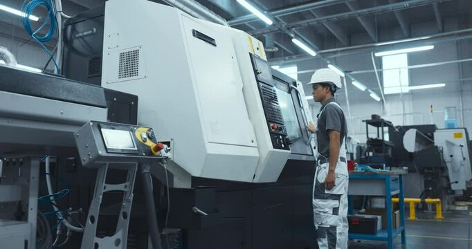 Asian Male Engineer in a White Hard Hat Operating a CNC Milling Machine in a Modern Factory. Young Technician Inserting Parameters into the Computer, Automating Production Line