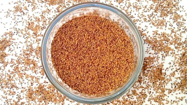 Fenugreek seeds in a glass bowl spices spilled around it, rotating on white background, center frame, top view, close up, herbs and spices.