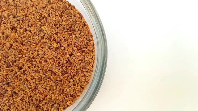 Half of circle shaped Fenugreek seeds glass bowl in the left half of the frame, rotating, isolated on the white background, closeup, herbs and spices.