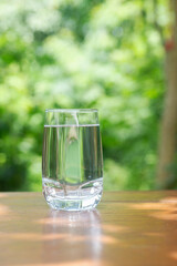 glass of drinking water on wooden table in in garden with green bokeh background.