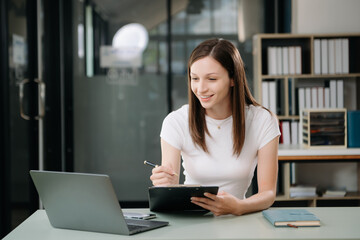 Fototapeta premium Beautiful woman using laptop and tablet while sitting at her working place. Concentrated