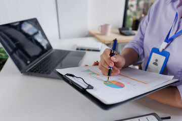 Close up of business woman or accountant hand holding pen working on calculator to calculate business data, accountancy document and laptop computer at office, business concept
