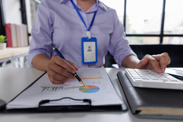 Close up of business woman or accountant hand holding pen working on calculator to calculate business data, accountancy document and laptop computer at office, business concept