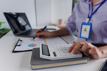 Close up of business woman or accountant hand holding pen working on calculator to calculate business data, accountancy document and laptop computer at office, business concept
