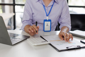 Close up of business woman or accountant hand holding pen working on calculator to calculate business data, accountancy document and laptop computer at office, business concept