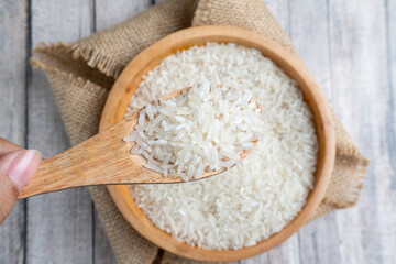 top view of hand holding a wooden spoon of rice with wooden bowl of rice on background