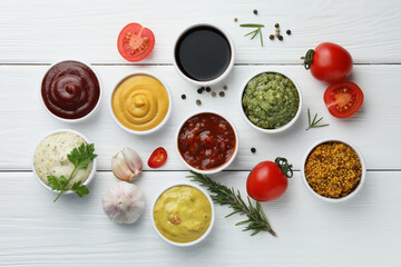 Many different sauces, spices and vegetables on white wooden table, flat lay