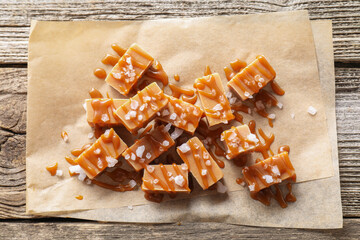 Yummy candies with caramel sauce and sea salt on wooden table, top view