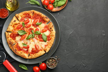 Delicious Margherita pizza, ingredients and cutter on black table, top view. Space for text