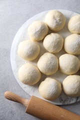 Raw dough balls and rolling pin on light grey table, top view