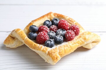 Tasty puff pastry with berries on white wooden table, closeup