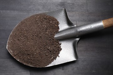 Metal shovel with soil on black wooden table, top view