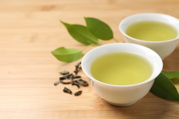 Refreshing green tea in cups and leaves on wooden table, closeup. Space for text