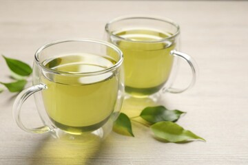Refreshing green tea in cups and leaves on wooden table, closeup
